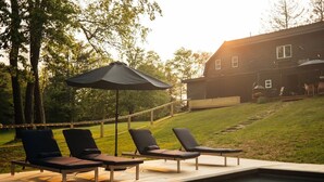 Ein Poolbereich mit Liegestühlen und Sonnenschirm, mit Blick auf eine Rasenfläche und ein Haus.