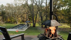 An outdoor deck with a fire feature, seating, and a view of a pond and trees. - Coop 004 Summary:<br>Wel (Kenoza Lake)