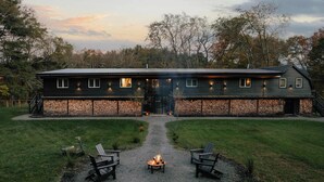 A large, dark wooden building with a fire pit in the center, surrounded by outdoor seating.