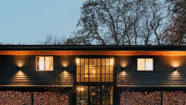 A modern building with a stone wall and a fire pit in the foreground.