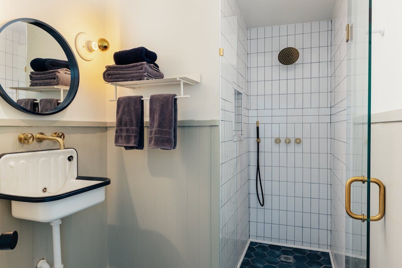 Een badkamer met een wit wastafelmeubel, een spiegel en een douche met een glazen deur.