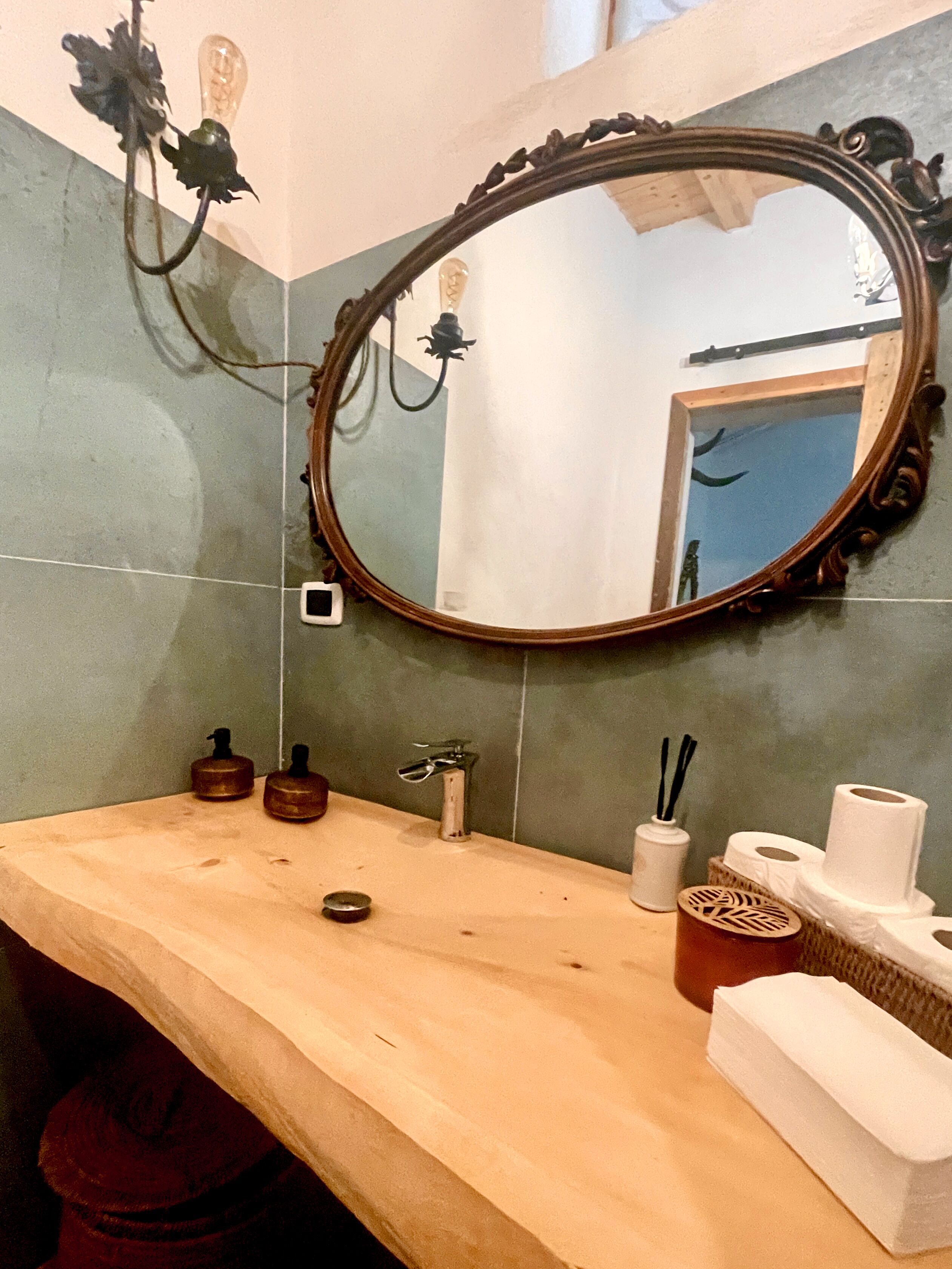 A bathroom with a wooden vanity, a large mirror, a light fixture, and toiletries.