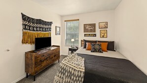 Un dormitorio con cama, cómoda, televisor y decoración en la pared.