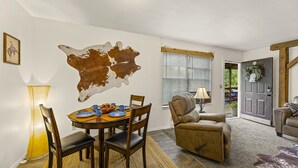 Un comedor con una mesa redonda, sillas, un mapa en la pared, una lámpara y una puerta que da al exterior.