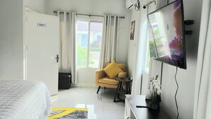 A hotel room with a bed, a TV, a ceiling fan, a sofa, a small table, and a window with curtains. - Cozy 3-bedroom villa w/ AC, pool & unlimited beach access 10 mins from Ocho Rios (Saint Ann's Bay)
