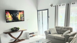A modern living room with a flat-screen TV, a ceiling fan, a sofa, a coffee table, and a shoe rack. - Cozy 3-bedroom villa w/ AC, pool & unlimited beach access 10 mins from Ocho Rios (Saint Ann's Bay)