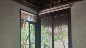 Una habitación con un amplio ventanal corredero que da a un espacio exterior con terraza de madera y una estructura de techo de paja.