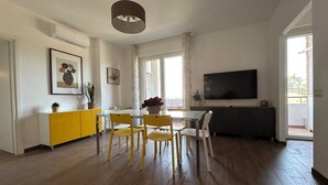 Un salon moderne avec un coin repas, comprenant un téléviseur à écran plat, un parquet et un meuble jaune.