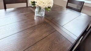 A dining table with a vase of white flowers, two chairs, and a painting on the wall.