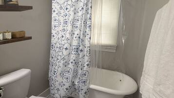 Ein Badezimmer mit Toilette, Badewanne, Duschvorhang, einem Fenster und einem Handtuchhalter.