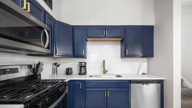 A modern kitchen with dark blue cabinets, a stainless steel stove, a microwave, and a dishwasher.