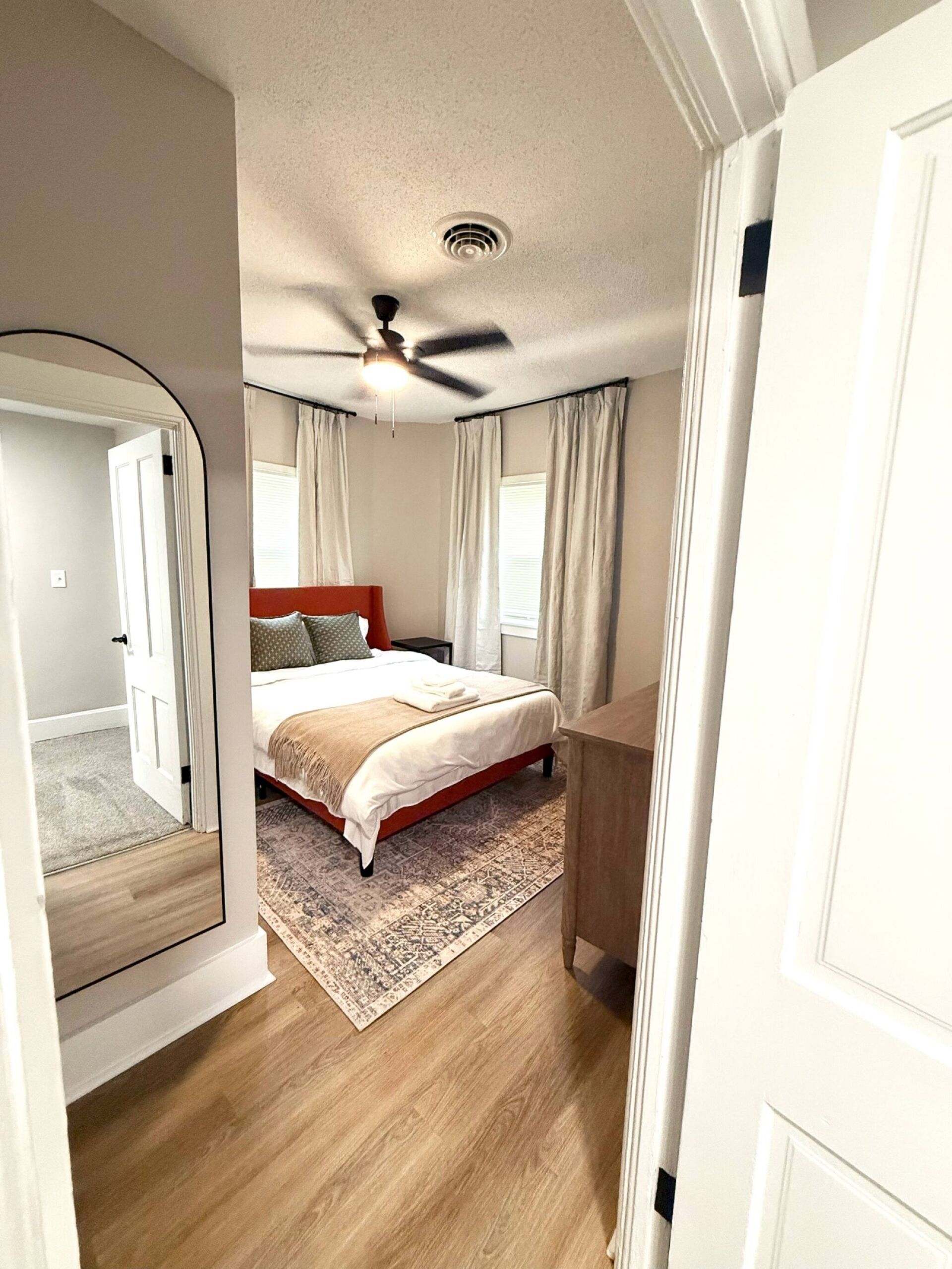 A bedroom with a bed, a ceiling fan, a window with curtains, and a wooden floor.