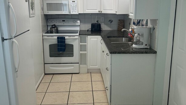 A compact kitchen with white cabinets, a microwave, an oven, and a toaster. - Emerald Palms Unit 2 (Englewood)