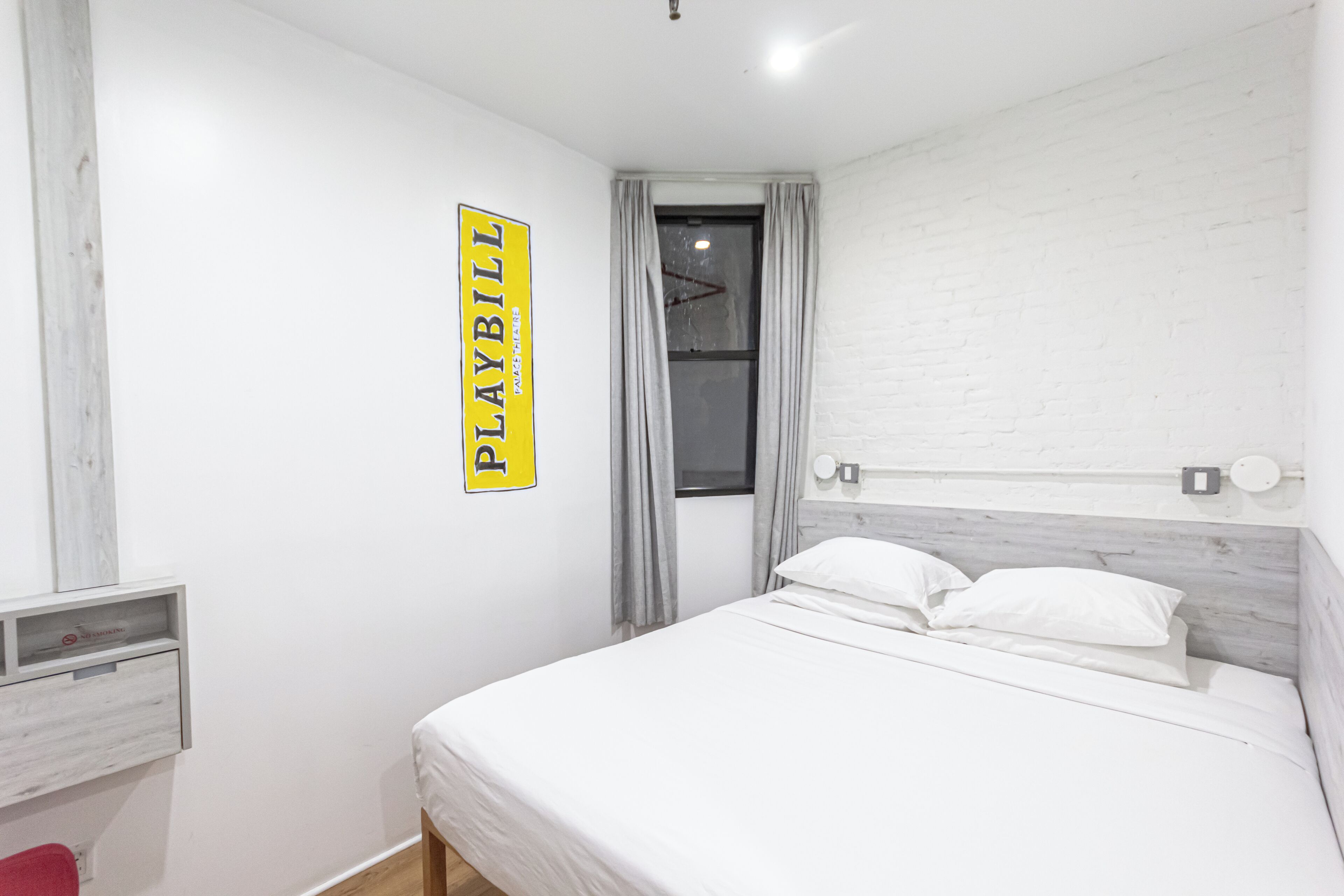 A bedroom with a bed, a wall-mounted sign, a window with curtains, and a white brick wall.