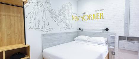 Una habitación de hotel con una cama, un estante de madera, un mural en la pared y una pared de ladrillo blanco con el texto 'THE NEW YORKER'.