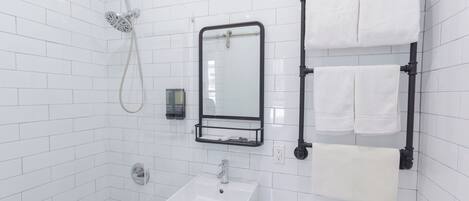 A bathroom with white tiled walls, a white sink, a mirror, a towel rack, and a showerhead.