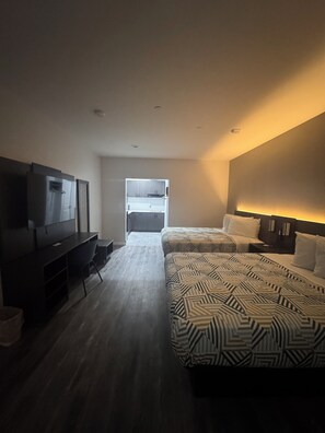 Habitación de hotel con dos camas, televisión, escritorio y vista al pasillo.