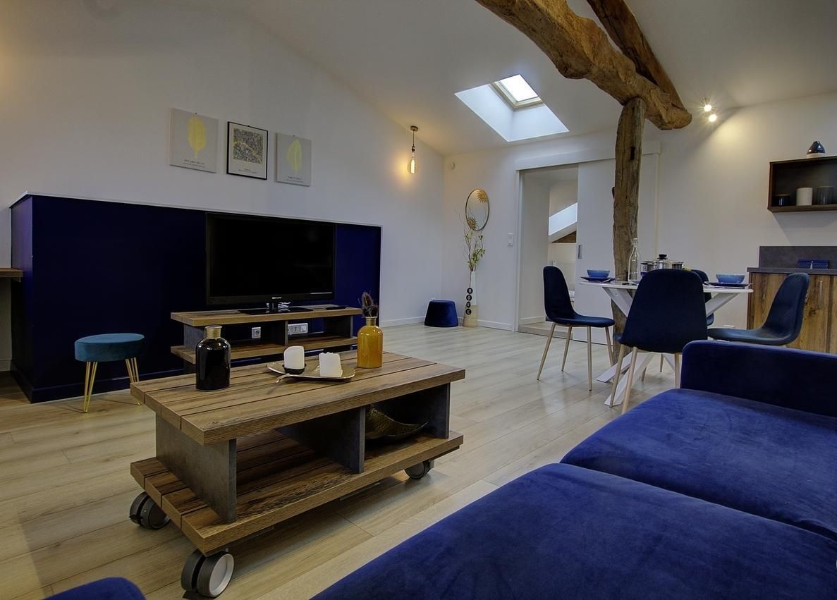 Uma sala de estar moderna com uma grande TV de tela plana, uma mesa de centro de madeira e um sofá azul.