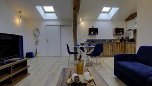 A modern living room with a TV, seating, and a dining area with a kitchen in the background.