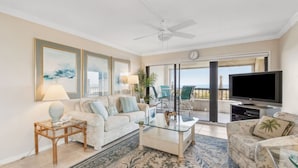 A living room with a sofa, coffee table, and TV. There is a balcony with a view.
