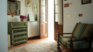 A room with a wooden dresser, a green armchair, a patterned rug, and a window with curtains. - Casa Linda a window to the sea (Sant' Anna di Stazzema)