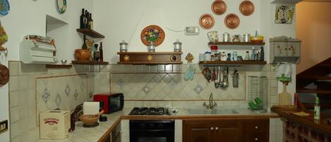 A kitchen with a stove, oven, sink, and various kitchen utensils. There are plates, bottles, and a clock on the wall.