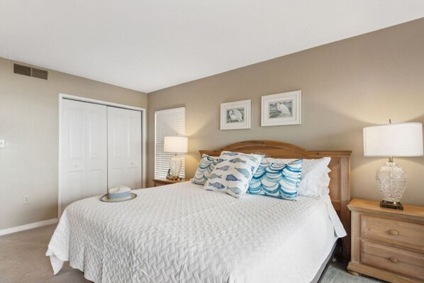 A bedroom with a large bed, a nightstand, a lamp, and two framed pictures on the wall.