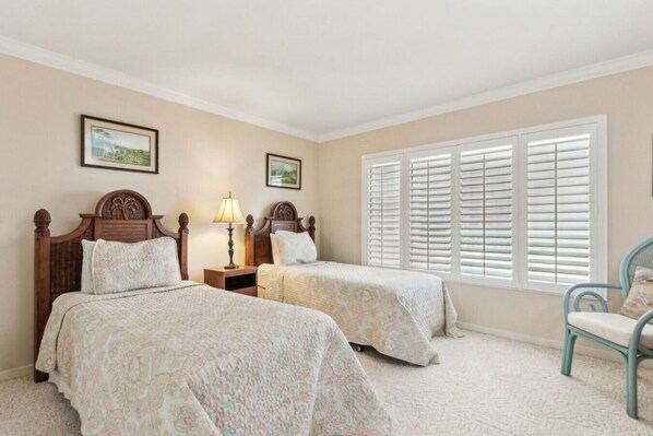 A bedroom with two beds, a nightstand, a lamp, a chair, and a window with shutters.