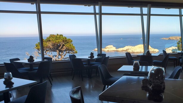 Un ristorante con tavoli e sedie, ampie finestre e vista sul mare.