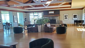 Un'ampia stanza con soffitto alto, travi in legno, un camino, un pianoforte e confortevoli zone relax.