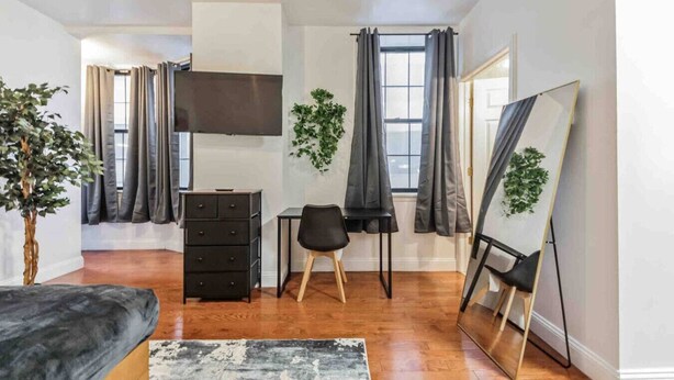 A modern bedroom with a bed, dresser, desk, chair, and a large mirror. - Studio Across the Street from Convention Center 2R (Philadelphia)