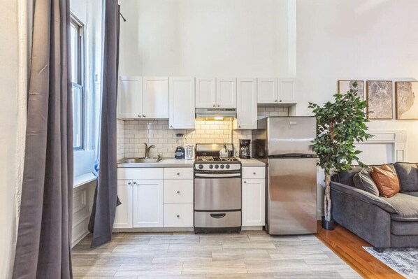 A compact kitchen with white cabinets, a stove, a refrigerator, and a coffee maker.