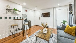 A modern living room with a sofa, a coffee table, and a small dining area with stools.
