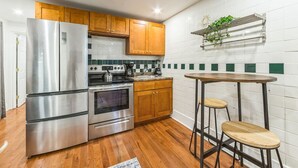 A modern kitchen with stainless steel appliances, wooden cabinets, and a small round table with stools.