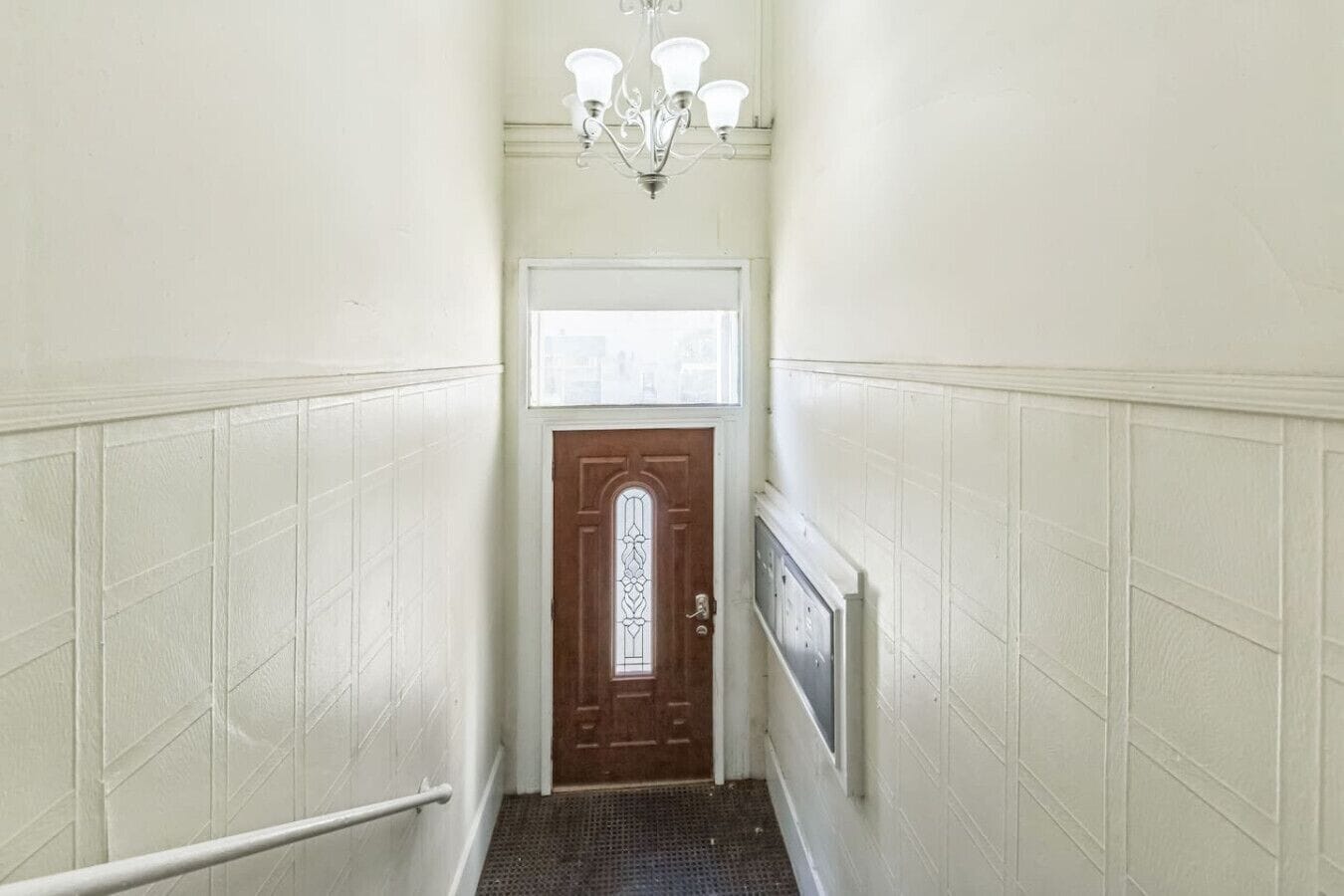 Ein schmaler Korridor mit weißer Wandverkleidung, einer Holztür mit Glasfeld und einem an der Wand befestigten Heizkörper.