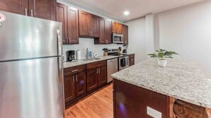Una cocina moderna con electrodomésticos de acero inoxidable, armarios de madera, encimeras de granito y una pequeña planta en maceta.