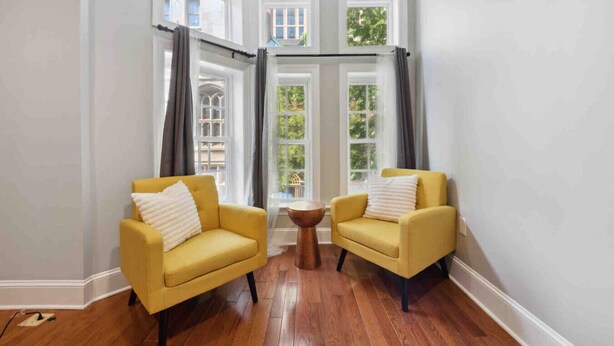 Una habitación con dos sillones amarillos, una mesita de madera y ventanas grandes con cortinas.