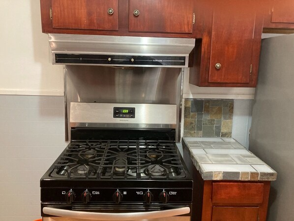 Una cocina con campana de acero inoxidable, estufa a gas y armarios de madera.
