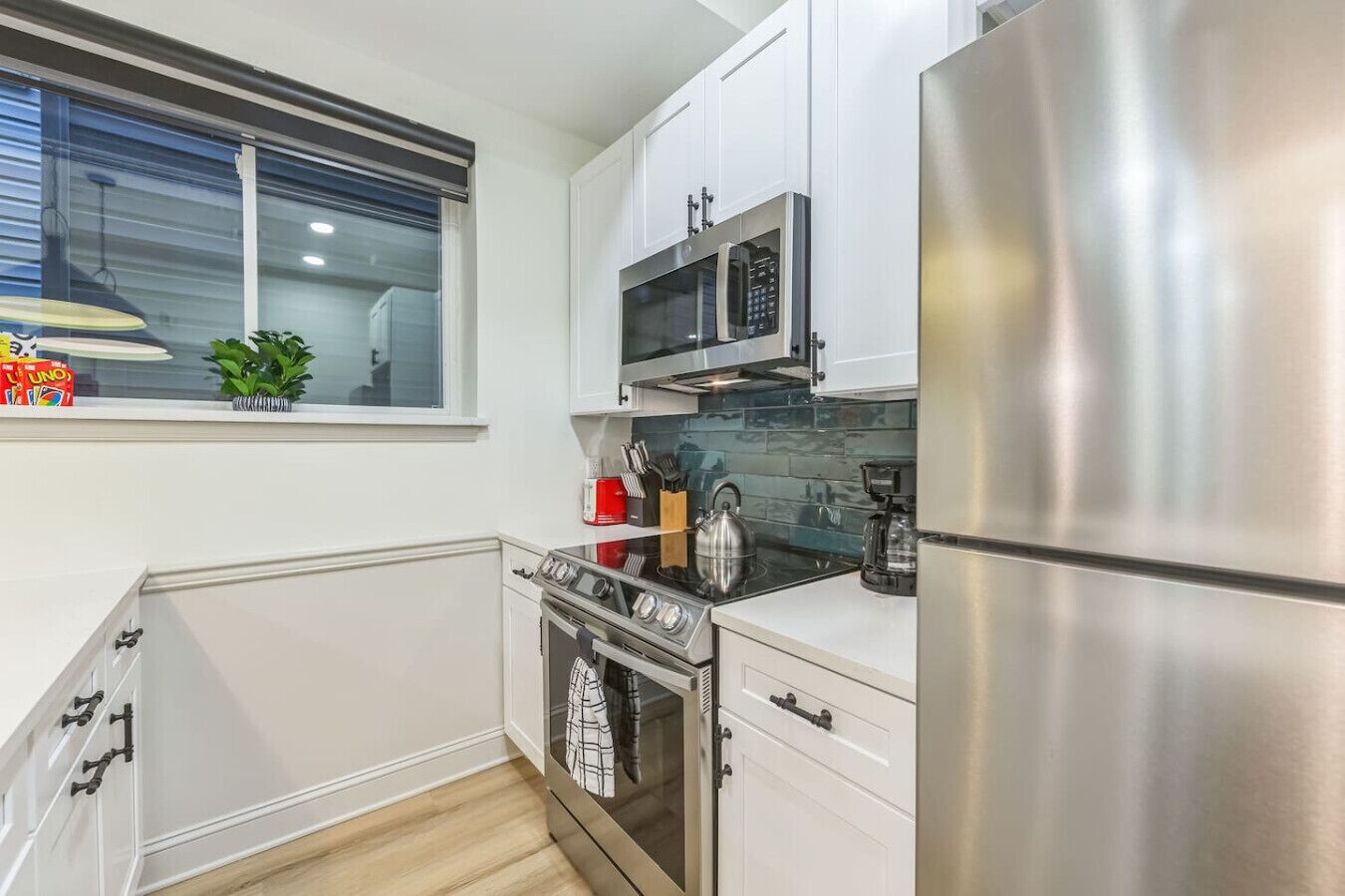 A modern kitchen with white cabinetry, a stainless steel refrigerator, a microwave, and a stove.