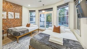 A modern hotel room with two beds, a brick accent wall, large windows, and a flat-screen TV. - New 2/2 Across from Fairmount Park | 10 mins to DT (Philadelphia)