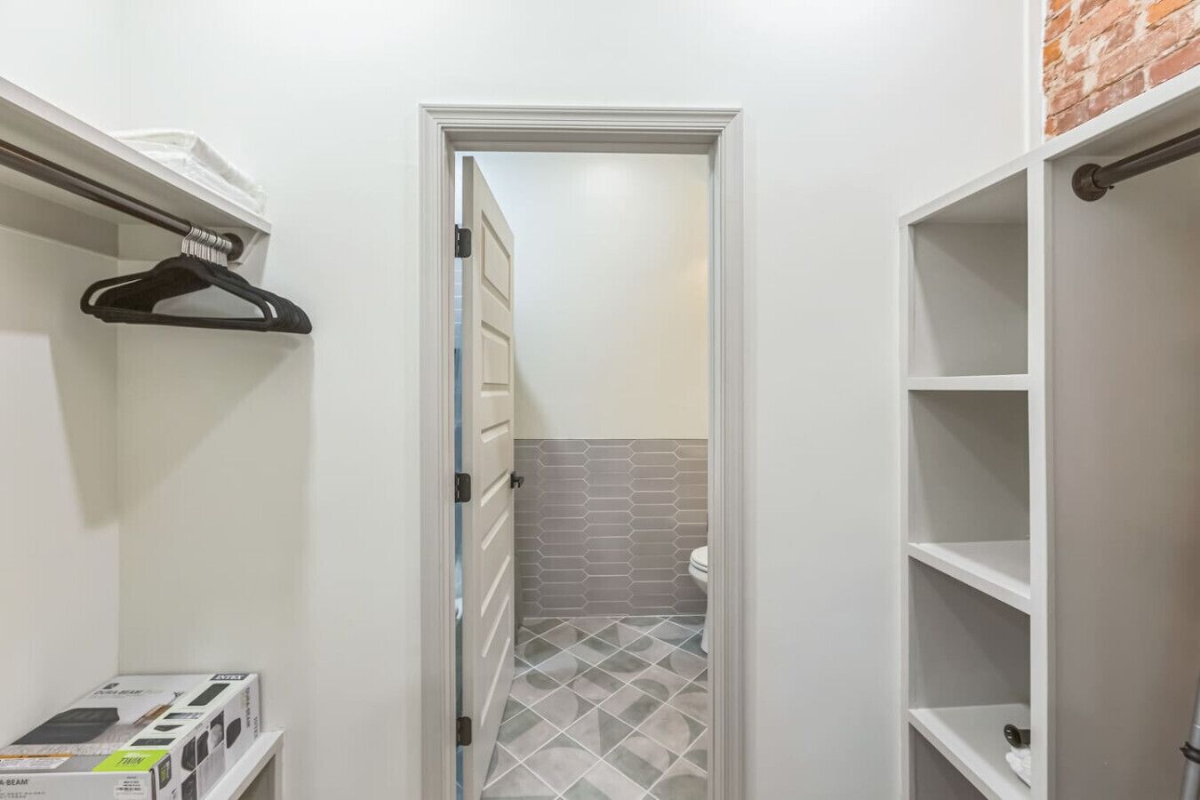 Un corridoio stretto con una porta bianca che dà su un bagno con piastrelle grigie e un water bianco.