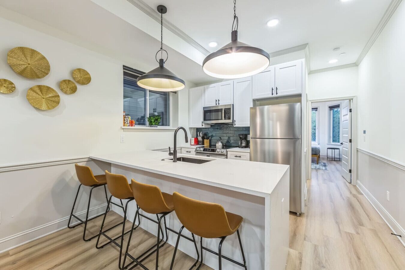 Una cocina moderna con una isla central, taburetes de bar, electrodomésticos de acero inoxidable y placas decorativas en la pared.