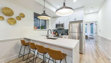 Una cocina moderna con una isla central, taburetes de bar, electrodomésticos de acero inoxidable y placas decorativas en la pared.