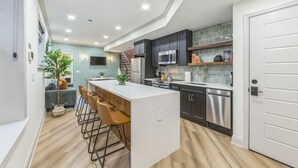 Uma cozinha moderna com ilha central, banquetas de bar, armários escuros e eletrodomésticos de aço inoxidável.