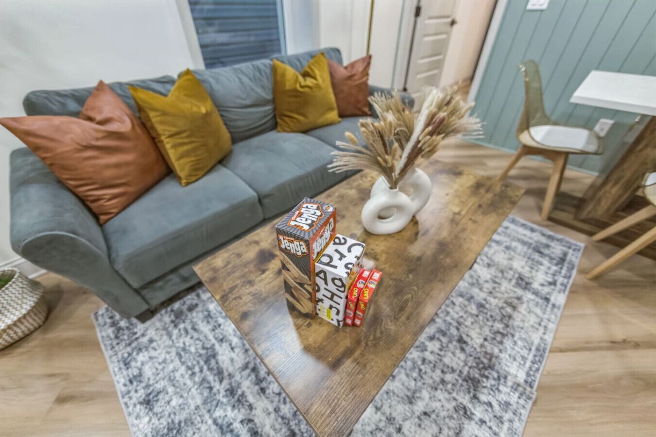Ein Wohnzimmer mit grauem Sofa, Holztisch und einer Vase mit Trockenpflanzen.