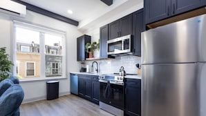 Una cocina moderna con armarios oscuros, electrodomésticos de acero inoxidable y un ventanal que proporciona luz natural.