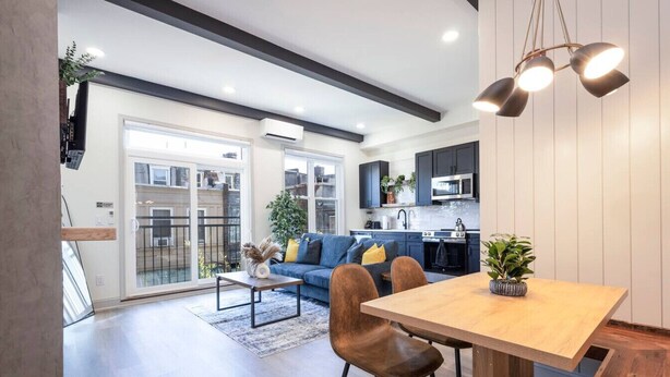 Una cocina moderna con armarios oscuros, una mesa de comedor de madera y una lámpara colgante.