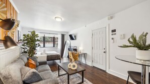 A modern living room with a grey sofa, a coffee table, and a dining area with a glass table and chairs.