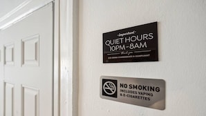 A door with two signs: one indicating quiet hours from 10 PM to 8 AM, and another prohibiting smoking, including vaping and e-cigarettes.