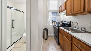 A modern kitchen with wooden cabinets, a stainless steel sink, and a glass shower enclosure.